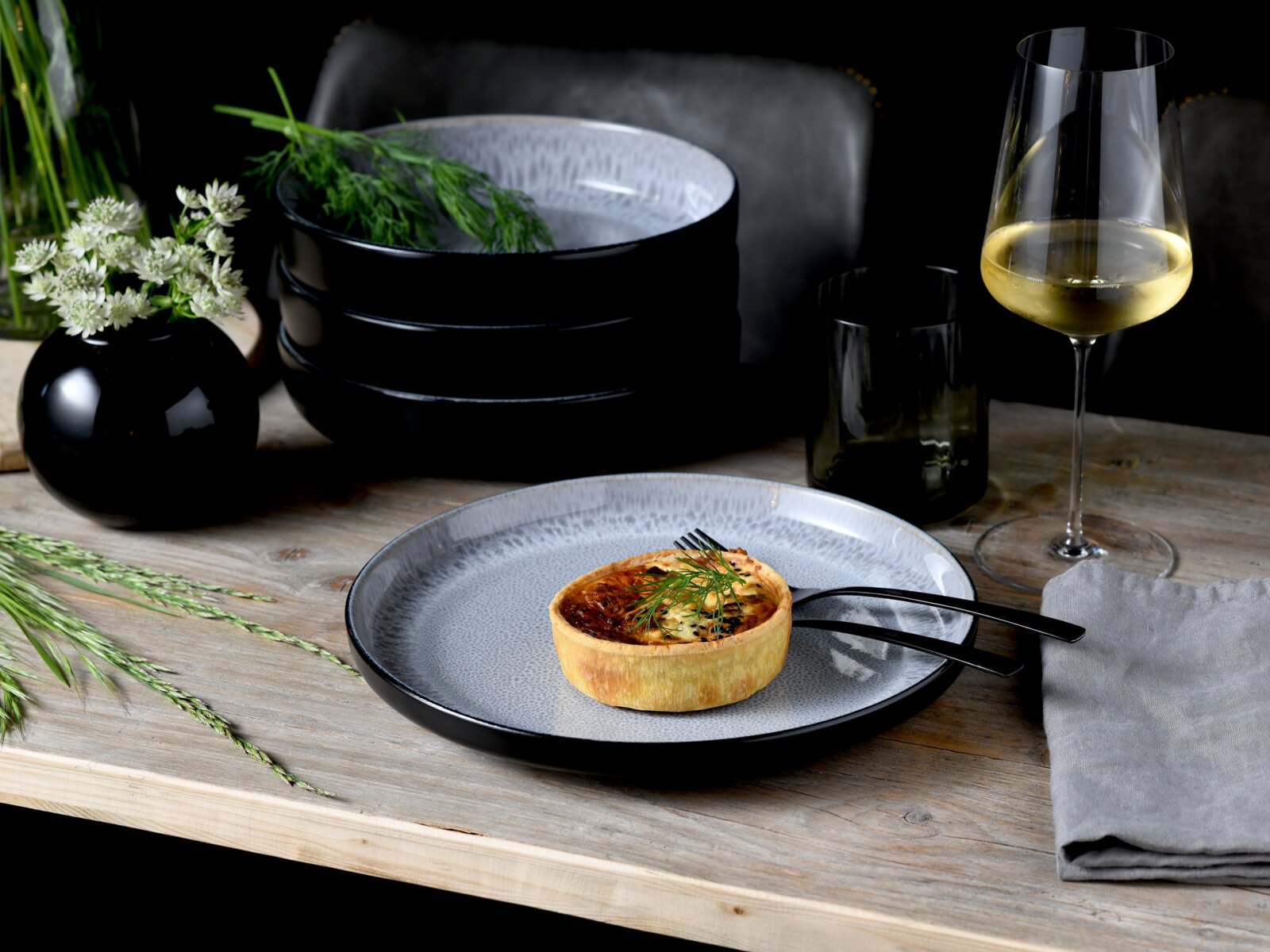 Creatable Tafelservice 12-tlg NORDIC FJORD Elegantes Tafelservice mit schwarzem und grauem Design, präsentiert auf einem Holztisch mit einem Quiche, Besteck, einem Weinglas und einer Vase mit Blumen, aus der Vogelperspektive.