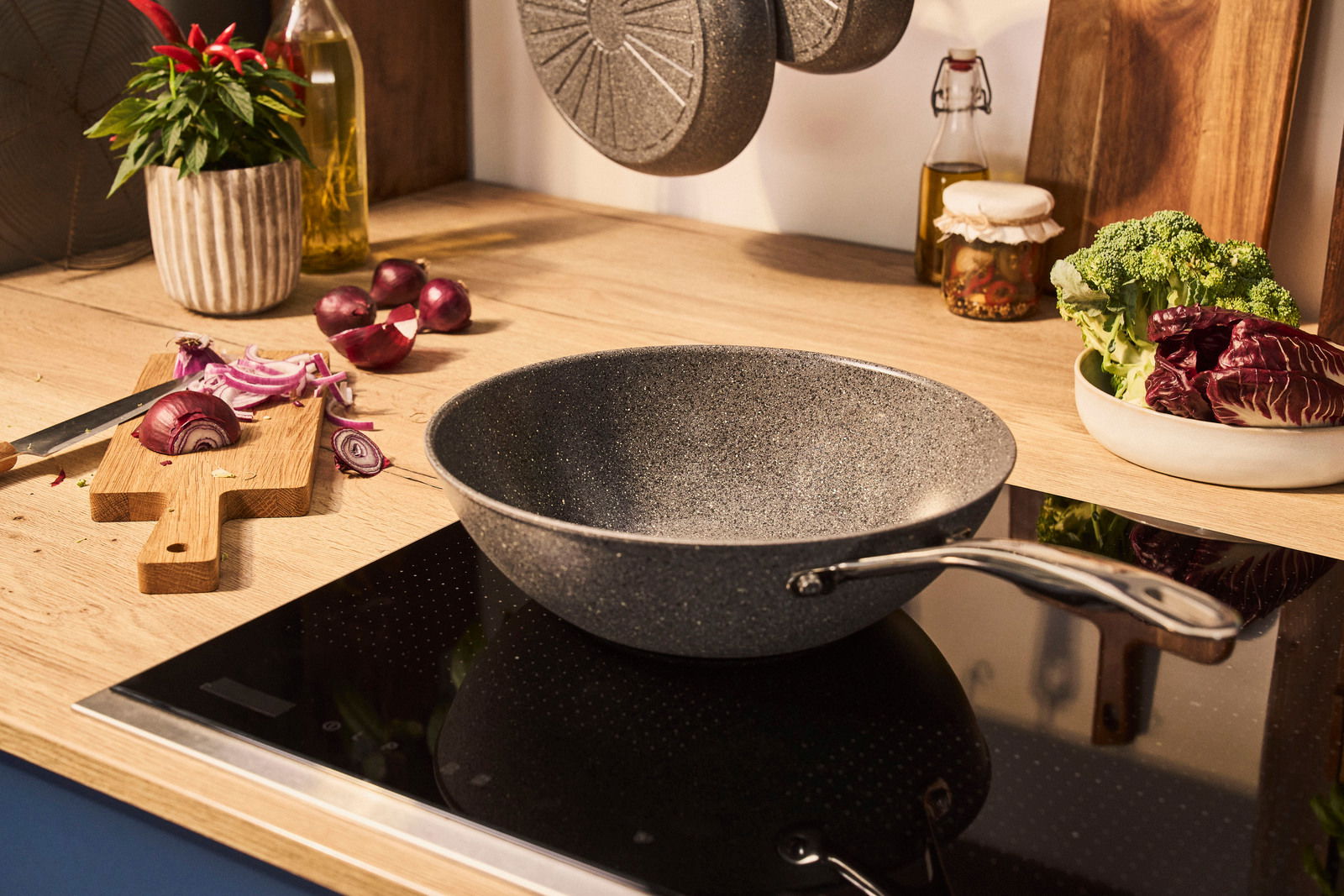 Wok mit 30 cm Durchmesser auf einem Herd, umgeben von frischem Gemüse und Küchenutensilien, aus seitlicher Perspektive.