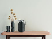 Isolierkanne Juwel in mattem Schwarz mit glänzendem Deckel, auf einem Holztisch neben modernen Vasen, seitliche Perspektive