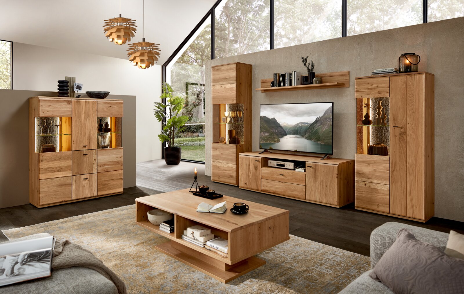 Cantus Highboard REIMS Wohnzimmer-Set aus hellem Massivholz mit TV-Lowboard, zwei Vitrinen mit LED-Beleuchtung, Sideboard, Wandregal und Couchtisch, gezeigt in frontaler Raumansicht mit leicht schräger Perspektive von links