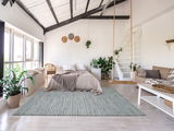 Moderner Wohnraum mit hellem Wollteppich in Pastelltönen, umgeben von Pflanzen und minimalistischer Einrichtung, aus der Perspektive eines offenen Raumes mit Blick auf das Bett und die Schaukel.