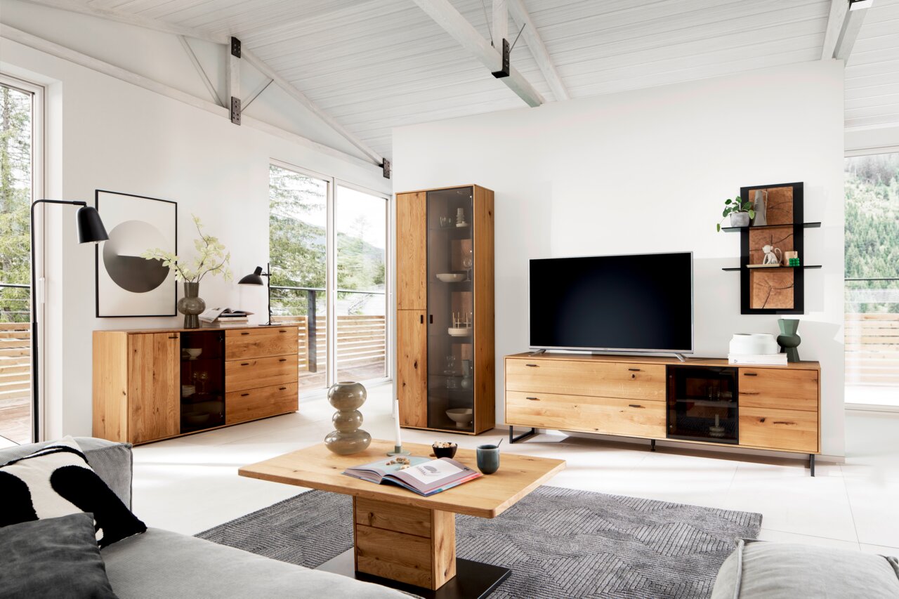 Moderner Couchtisch aus Holz in einem hellen Wohnzimmer, frontal von vorne fotografiert, umgeben von stilvollen Möbeln und großen Fenstern mit Blick ins Grüne.