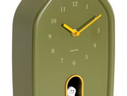 Grüne Wanduhr mit gelben Zeigern und einer kleinen Hundefigur in einer Öffnung unten, seitliche Perspektive