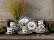 Klassisches Porzellan-Geschirrset mit braunem floralem Randdekor und Jagdmotiven (Hirsch, Fuchs) sowie passenden Tassen und Tellern, frontal aus leicht erhöhter Perspektive vor rustikaler Holzwand inszeniert