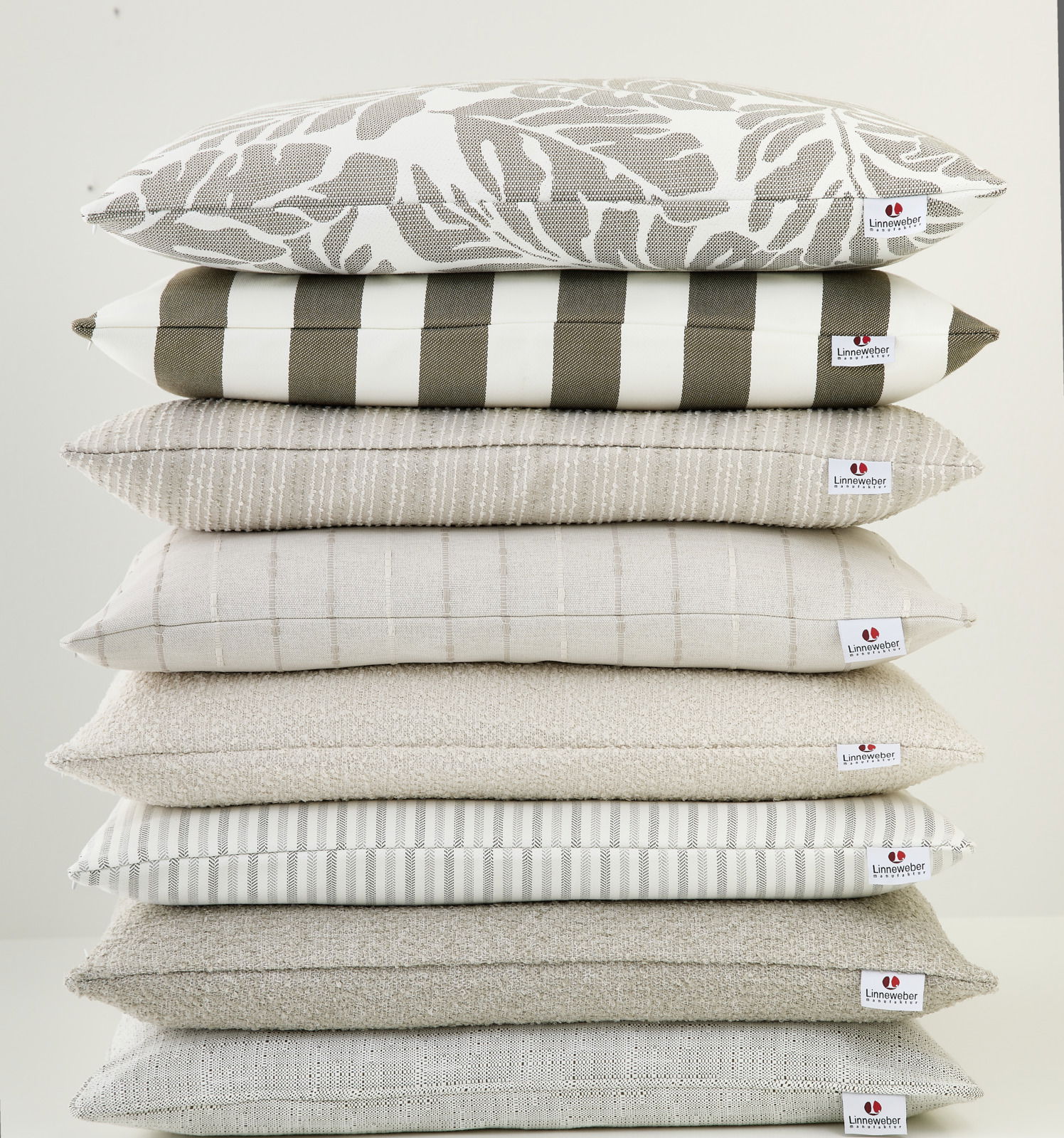 Stapel von Outdoor-Kissen in verschiedenen Mustern und neutralen Farben, seitliche Perspektive