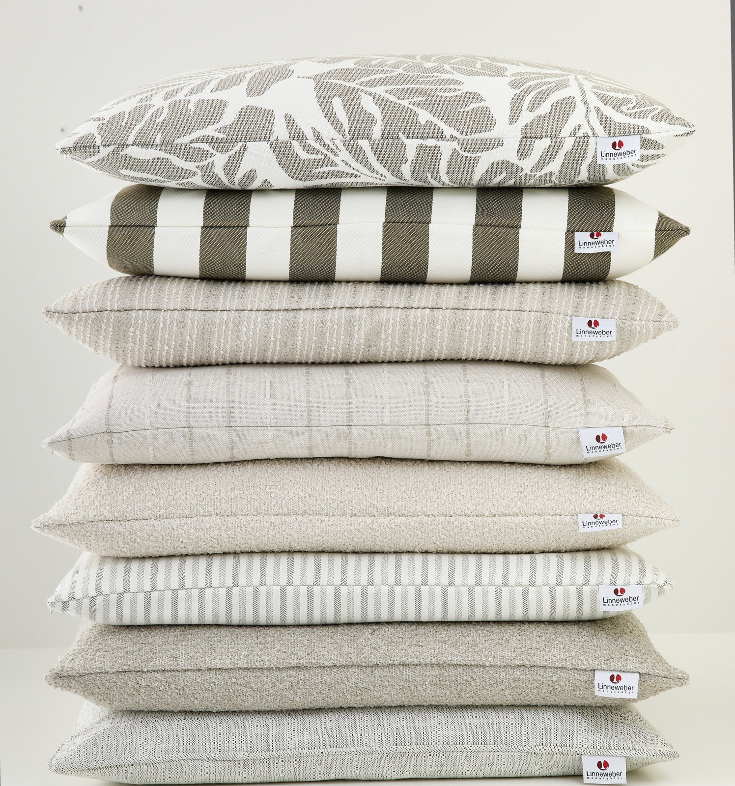 Stapel von Outdoor-Kissen in verschiedenen Mustern und neutralen Farben, seitliche Perspektive