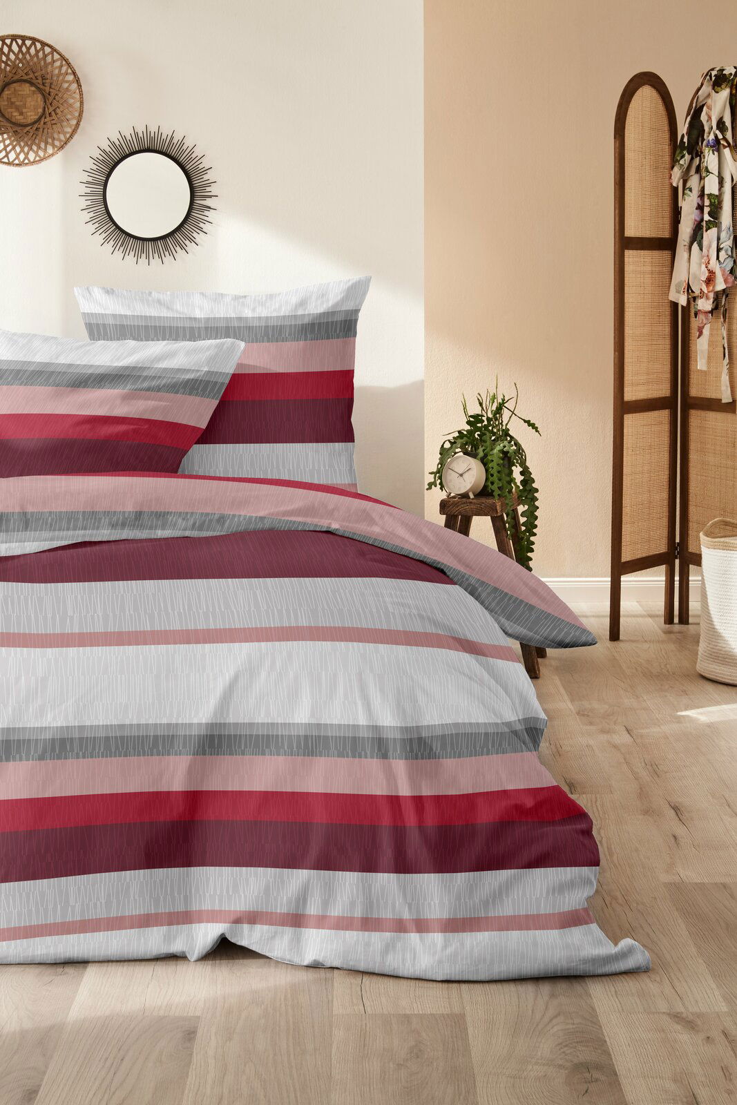 Bettwäsche-Set mit Streifenmuster in Rot- und Grautönen, auf einem Bett in einem stilvoll eingerichteten Raum, aus der Vorderansicht fotografiert.