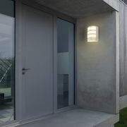 Moderne Akku-Außenwandleuchte von Briloner, montiert an einer Hauswand neben einer Tür, in eingeschaltetem Zustand bei Dämmerung.