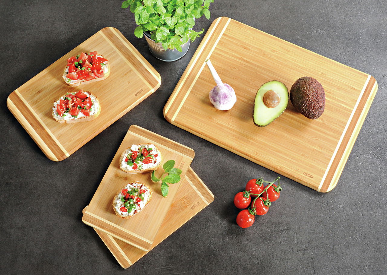 Vogelperspektive auf ein 4er-Set Bambus-Schneidebretter mit frischen Zutaten wie Avocado, Knoblauch und Tomaten.