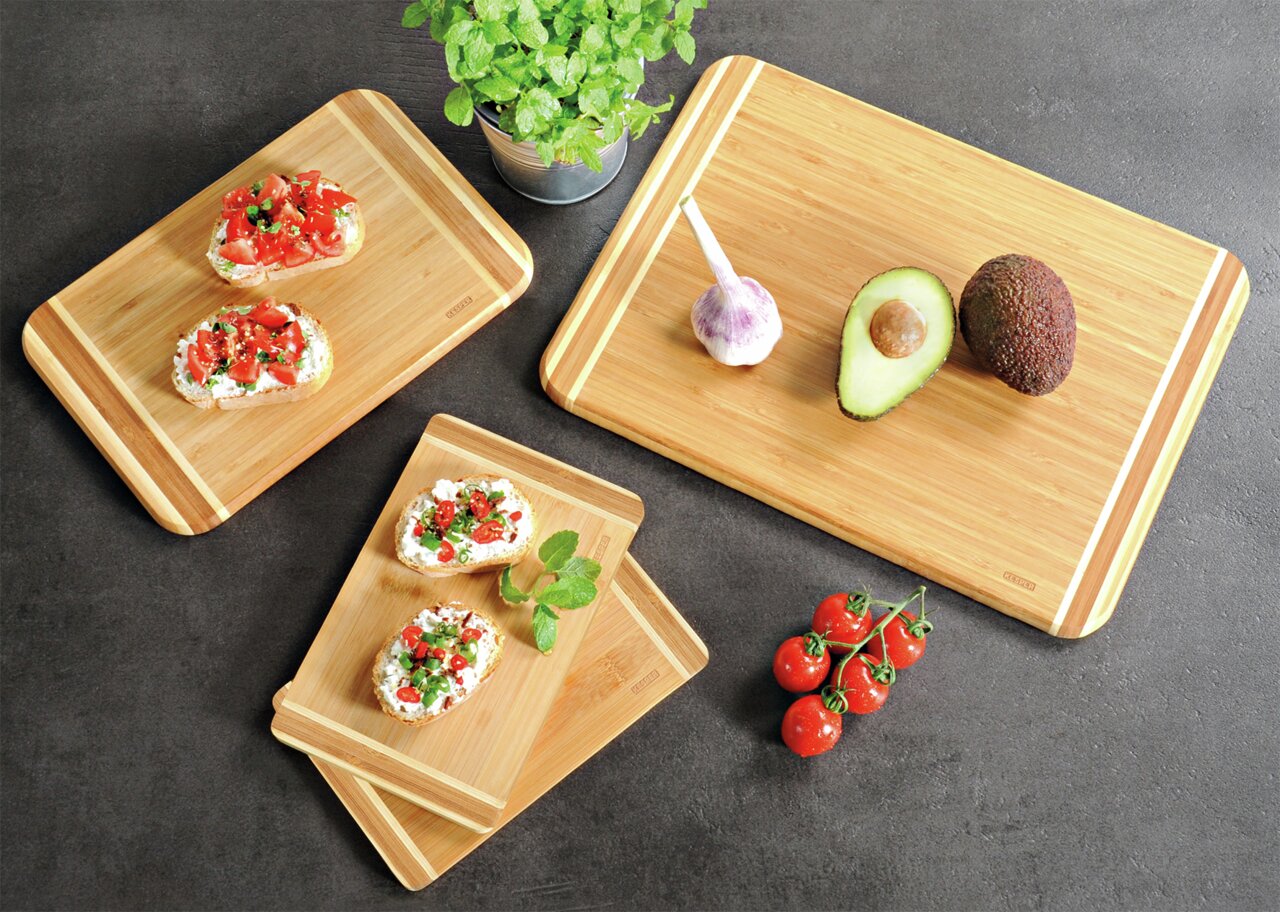 Vogelperspektive auf ein 4er-Set Bambus-Schneidebretter mit frischen Zutaten wie Avocado, Knoblauch und Tomaten.