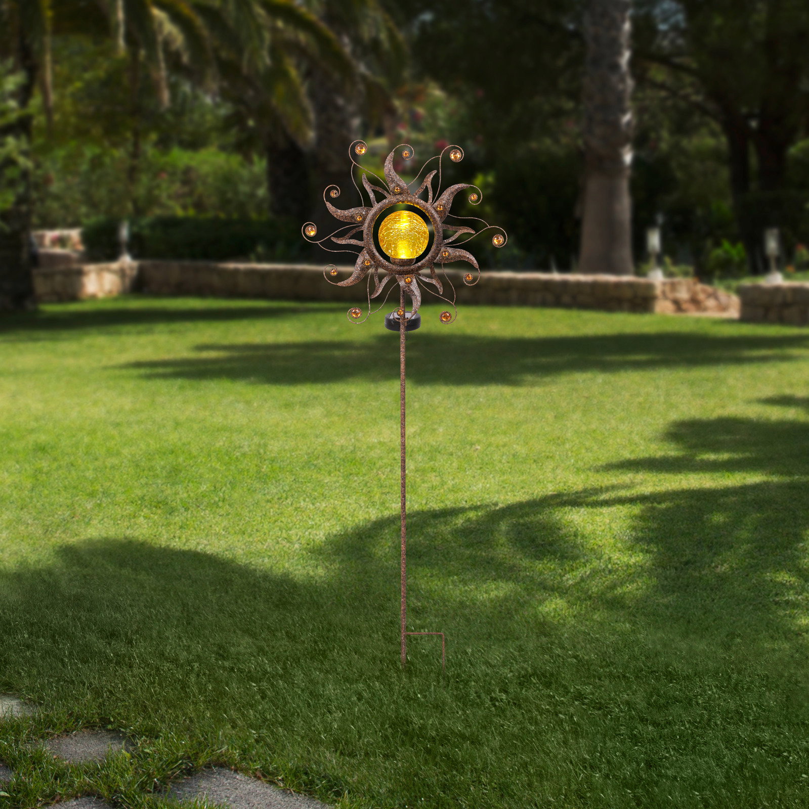 Solarleuchte in Form einer Sonne mit dekorativen Elementen, aufgestellt in einem Garten, seitliche Perspektive