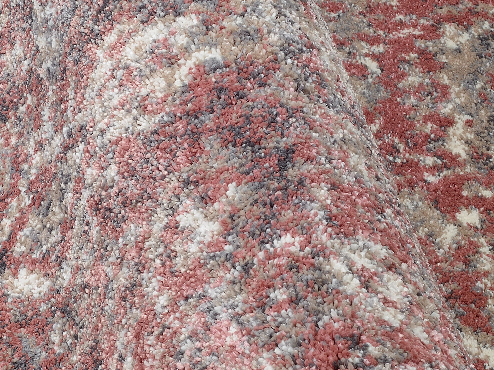 Nahaufnahme eines Designer-Teppichs mit gemusterten Farben in Rot-, Grau- und Beigetönen, aus seitlicher Perspektive aufgenommen.