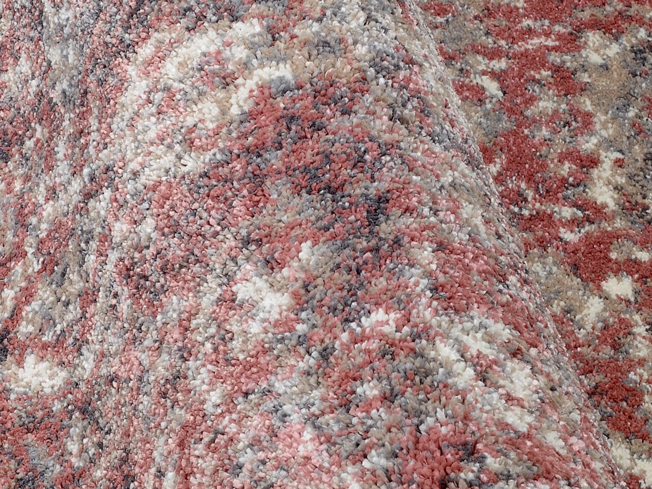 Nahaufnahme eines Designer-Teppichs mit gemusterten Farben in Rot-, Grau- und Beigetönen, aus seitlicher Perspektive aufgenommen.