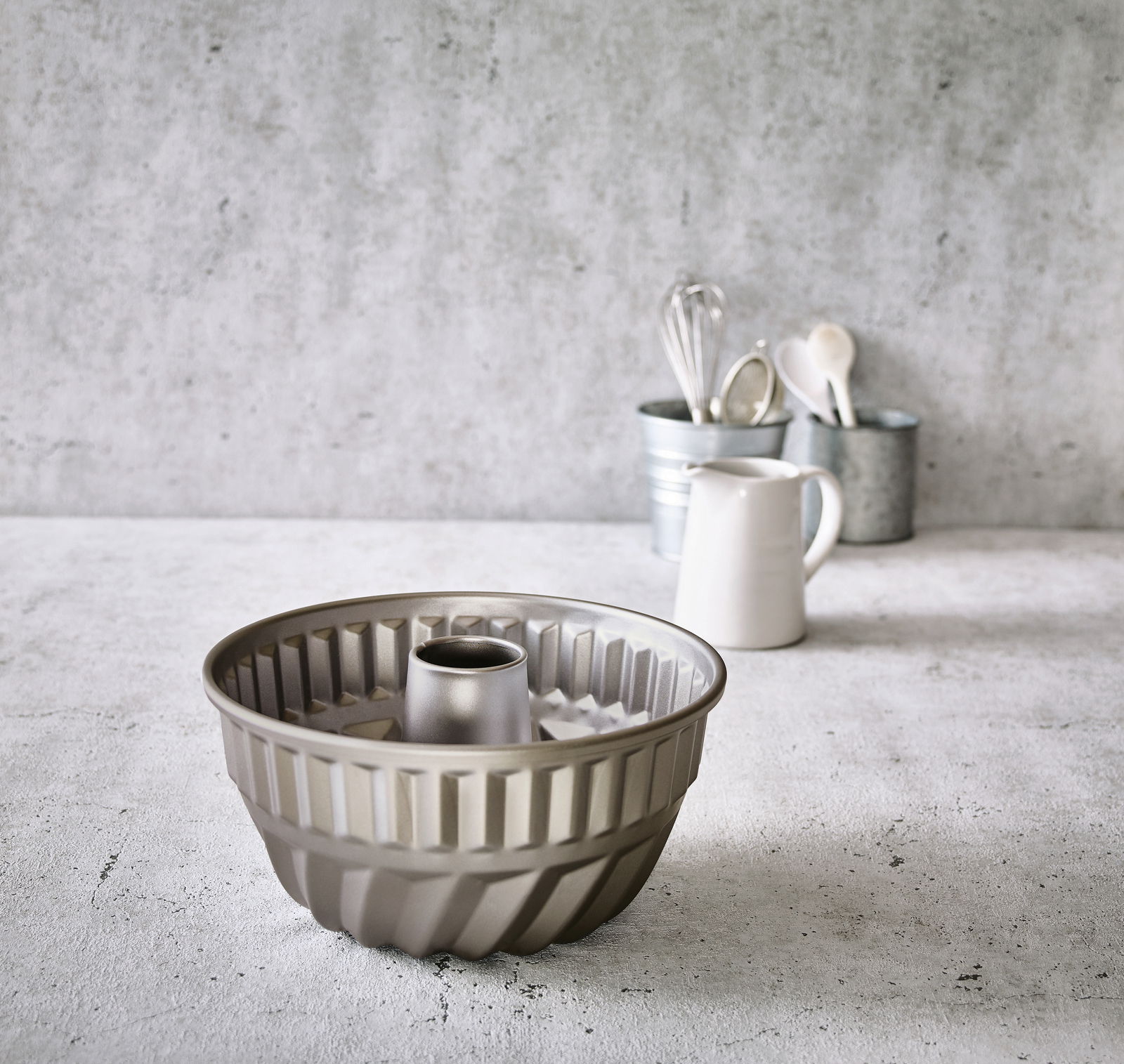 Birkmann Gugelhupfform BASIC BAKING Gugelhupfform aus Metall mit einem Durchmesser von 24 cm, auf einer Küchenarbeitsplatte stehend, im Hintergrund Küchengeräte und ein Krug. Perspektive von vorne.