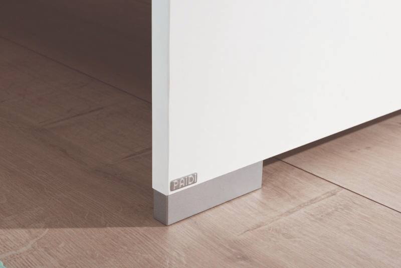 Nahaufnahme einer weißen Möbelkante mit grauem Sockel auf Holzboden, perspektivisch von der Seite aufgenommen.