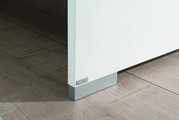 Nahaufnahme einer weißen Möbelkante mit grauem Sockel auf Holzboden, perspektivisch von der Seite aufgenommen.
