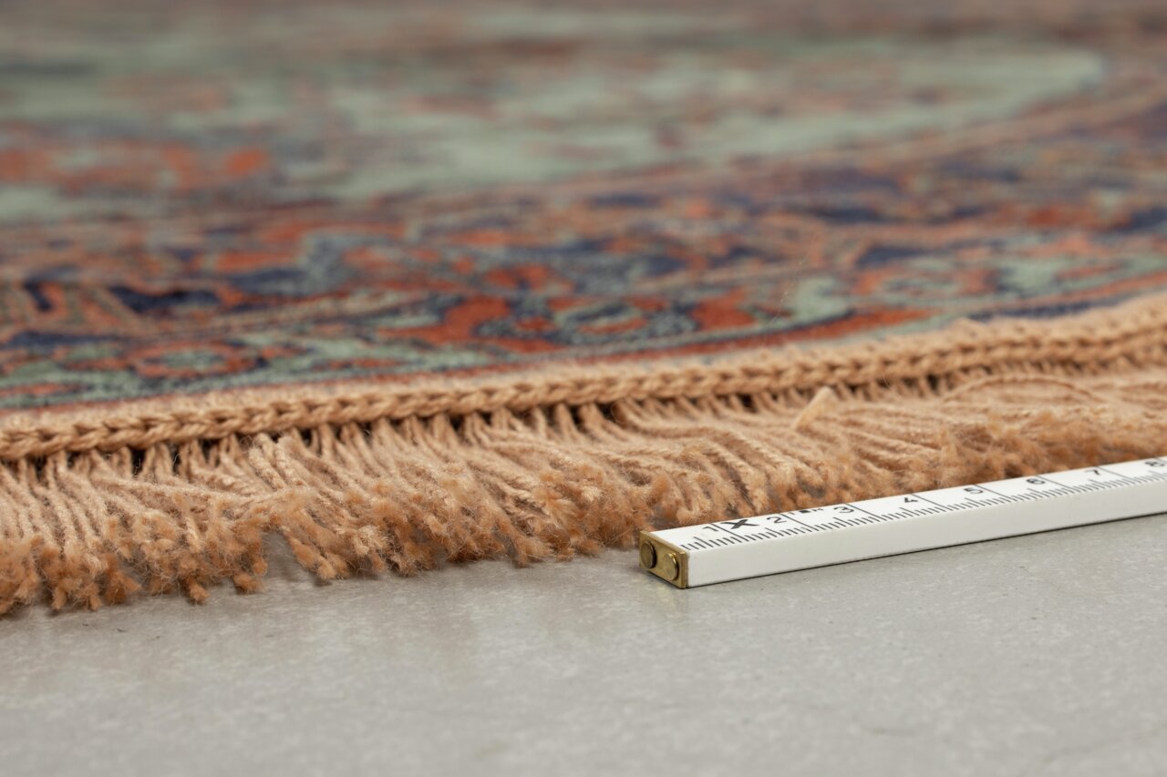 Nahaufnahme eines Teppichs mit Fransen und einem Maßband zur Größenbestimmung, seitliche Perspektive.