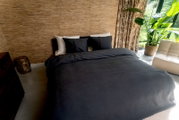 Blick auf ein stilvoll eingerichtetes Schlafzimmer mit einem Bett, das mit dunkelgrauer Bettwäsche in der Größe 135x200cm bezogen ist. Im Hintergrund sind eine beige Wand, Vorhänge und eine große grüne Pflanze zu sehen.