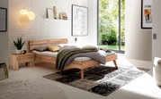 Modernes Schlafzimmer mit einem Kopfteil aus Holz und Metall, seitliche Perspektive. Das Bett ist mit Kissen und einer Decke dekoriert, umgeben von stilvollen Accessoires und einem großen Fenster mit Blick ins Grüne.