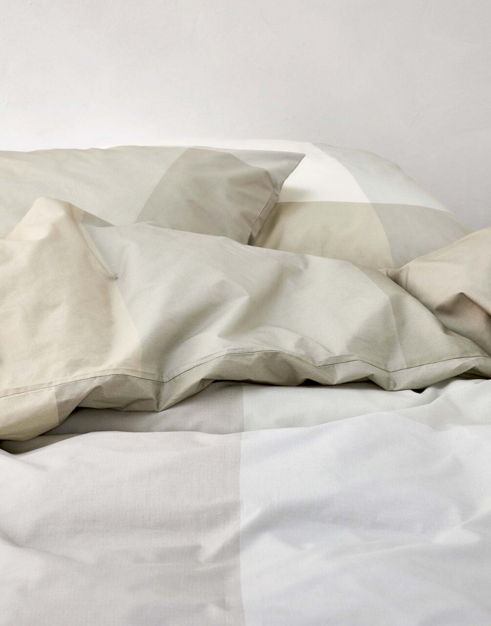 Nahaufnahme von Bettwäsche in sanften Beige- und Grautönen mit geometrischem Muster.