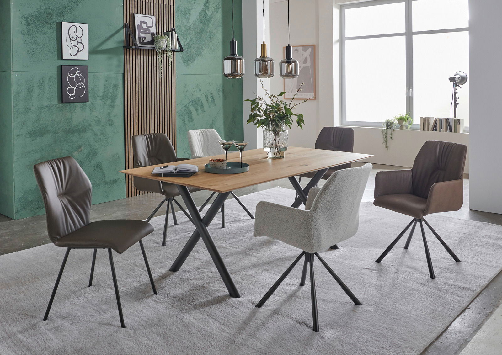 Moderner Esstisch mit Holzplatte und schwarzen Metallbeinen, umgeben von verschiedenen Stühlen in einem stilvoll eingerichteten Raum. Perspektive: seitlich.