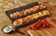 Een bakplaat met twee belegde baguettes, van bovenaf gefotografeerd, op een houten tafel met tomaten en dip.