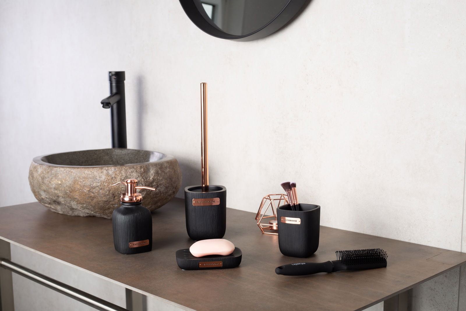 Moderne WC-Bürstengarnitur Kelsey in Schwarz mit Kupferakzenten, präsentiert auf einem Badezimmerwaschtisch aus Stein, seitliche Perspektive.