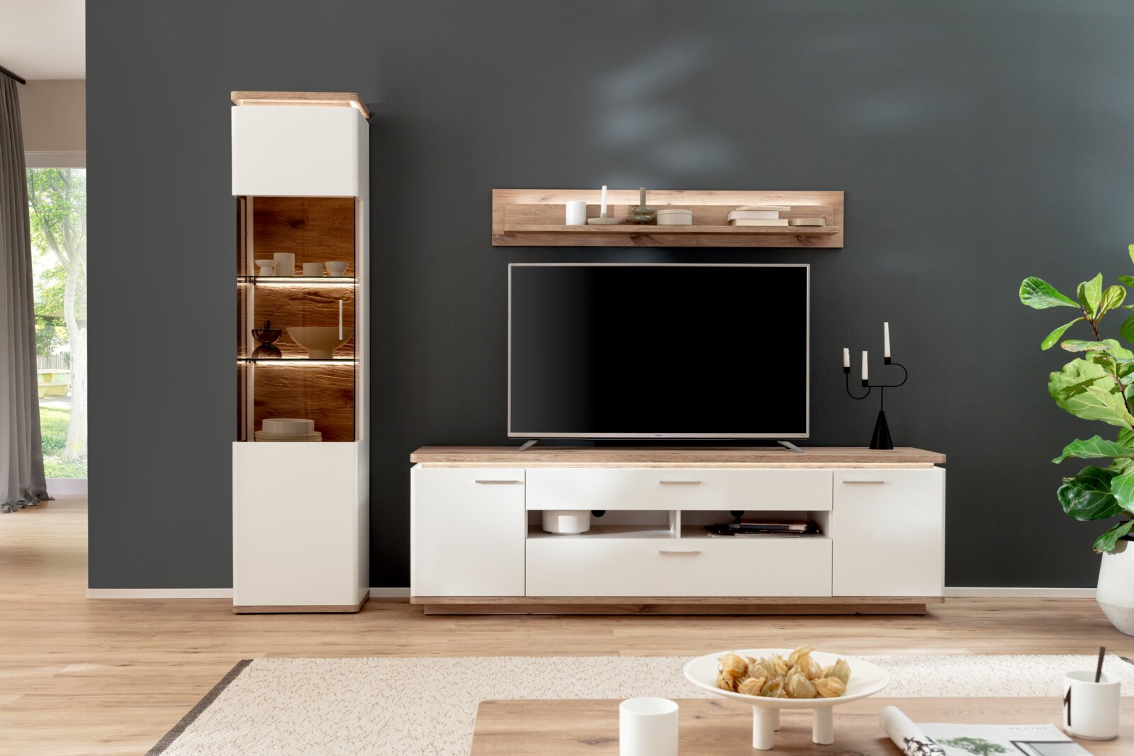 Wohnzimmermöbel-Set mit TV-Lowboard in Weiß und Holzoptik, Wandboard und hoher Vitrine mit Glasfront und Beleuchtung, frontale Perspektive