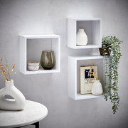 Dreiteiliges Wandregal-Set in Weiß, dekoriert mit Vasen, einem Buch und einer hängenden Pflanze, aus seitlicher Perspektive fotografiert.
