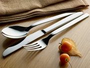 Elegantes Besteck-Set bestehend aus Löffel, Messer und Gabel auf einem Holztisch, mit dekorativen Physalis und Stoffservietten im Hintergrund, aus der Vogelperspektive fotografiert.