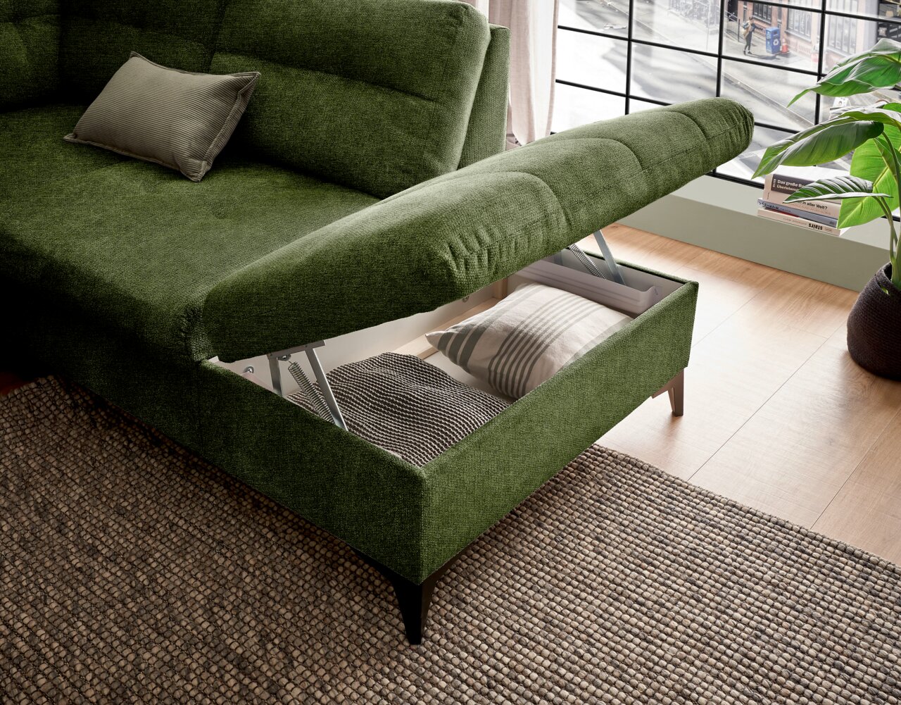 Grünes Ecksofa mit Stauraum, geöffnet, von schräg oben fotografiert, zeigt Kissen und Decke im Stauraum.