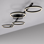 Moderne schwarze LED-Deckenleuchte mit vier ringförmigen Lichtkreisen an einer geraden Schiene, warmweiß leuchtend, fotografiert aus der Untersicht in schräger Perspektive.
