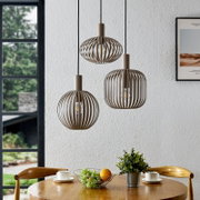 Drei moderne Pendelleuchten mit offenem, lamellenförmigem Schirm in Taupe/Beige hängen über einem Holztisch in einem Esszimmer; Perspektive: frontale Innenraumaufnahme auf Augenhöhe.