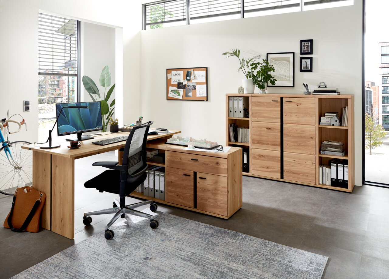 Linea Natura Aktenregal schmal/niedrig SONOS Büroeinrichtung mit Schreibtisch, Rollcontainer und Aktenschrank aus Holz in einem modernen, hellen Raum. Perspektive von vorne links.