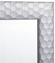 Nahaufnahme eines Spiegels mit einem silbernen, geometrisch gemusterten Rahmen, Perspektive von der Ecke.