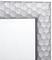 Nahaufnahme eines Spiegels mit einem silbernen, geometrisch gemusterten Rahmen, Perspektive von der Ecke.