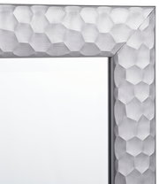 Nahaufnahme eines Spiegels mit einem silbernen, geometrisch gemusterten Rahmen, Perspektive von der Ecke.