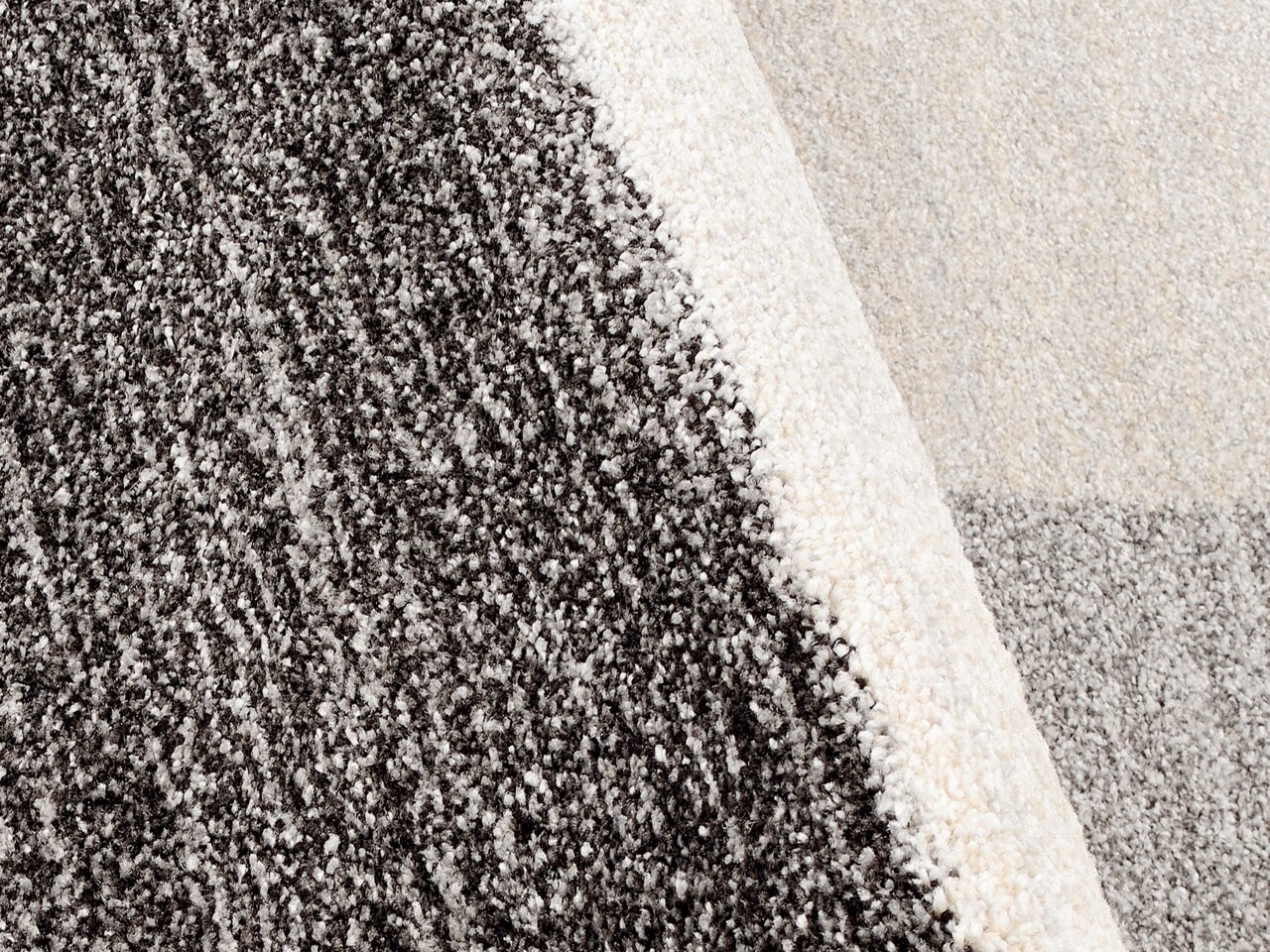 Nahaufnahme eines Teppichs mit gemustertem Design in Grautönen, perspektivisch von oben fotografiert.