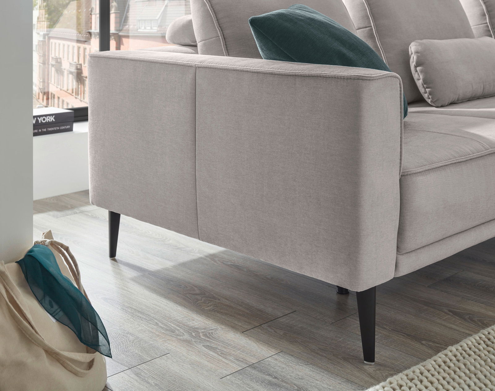 Rundecke in hellem Stoff mit schwarzen Beinen, seitliche Perspektive, dekoriert mit einem grünen Kissen.