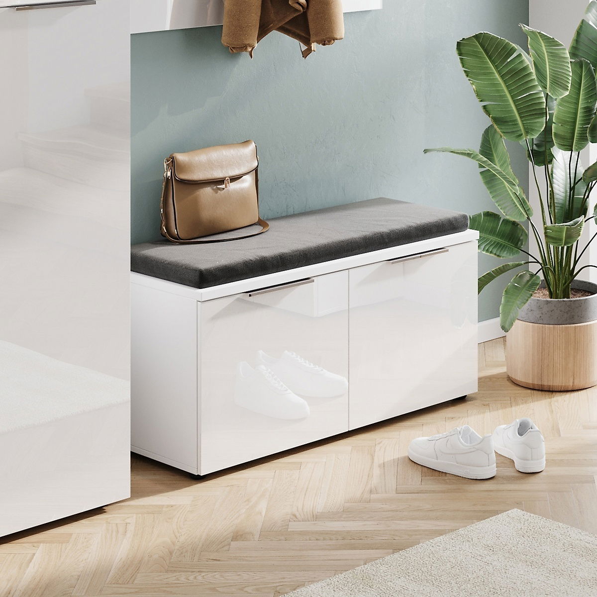Moderne Garderobenbank mit weißem Hochglanz-Finish und grauem Sitzkissen, seitliche Perspektive, dekoriert mit einer Tasche und umgeben von Pflanzen.