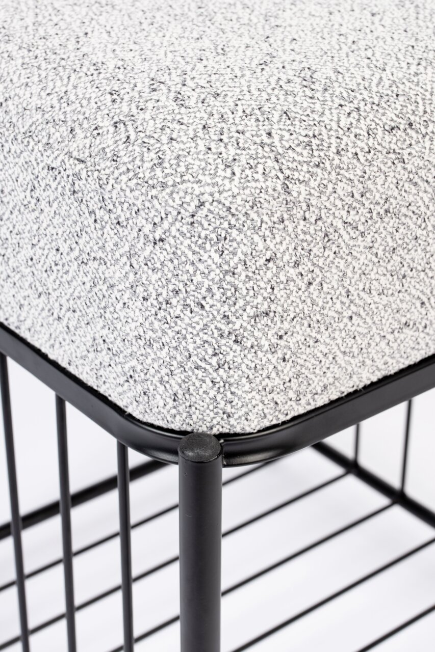 Close-up van een kruk met grijze stoffen bekleding en een zwart metalen frame, gezien vanaf de zijkant.