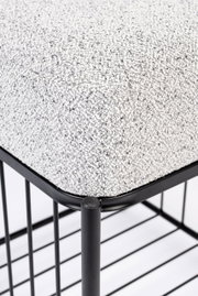 Close-up van een kruk met grijze stoffen bekleding en een zwart metalen frame, gezien vanaf de zijkant.