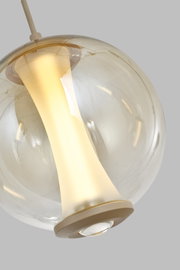 Close-up vanuit onderaanzicht van een moderne hanglamp met transparante glazen bol en warm verlichte, goudkleurige binnenkap