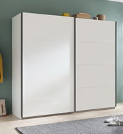 Moderner weißer Schwebetürenschrank mit zwei Türen, seitliche Perspektive, auf hellem Holzboden vor einer grünen Wand.