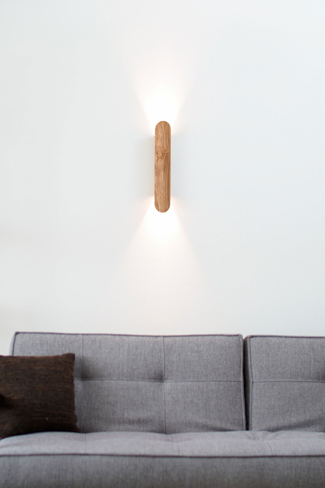 Zurbrüggen LED-wandlamp COLOMBIA LED-Wandleuchte aus Holz, montiert über einem grauen Sofa, mit Lichtstrahlen nach oben und unten, aus frontaler Perspektive.