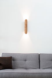 LED-Wandleuchte aus Holz, montiert über einem grauen Sofa, mit Lichtstrahlen nach oben und unten, aus frontaler Perspektive.