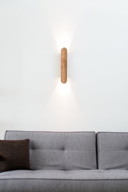 LED-Wandleuchte aus Holz, montiert über einem grauen Sofa, mit Lichtstrahlen nach oben und unten, aus frontaler Perspektive.
