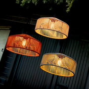 Drei hängende Pendelleuchten mit zylindrischen, geflochtenen Lampenschirmen in Natur- und Terrakotta-Tönen, warm leuchtend, in schräger Untersicht vor dunkler Wand.