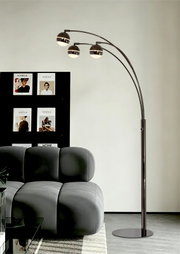 Moderne zwarte boogvloerlamp met drie gebogen armen en bolvormige lampenkappen, vanuit schuin vooraanzicht naast een grijze bank weergegeven