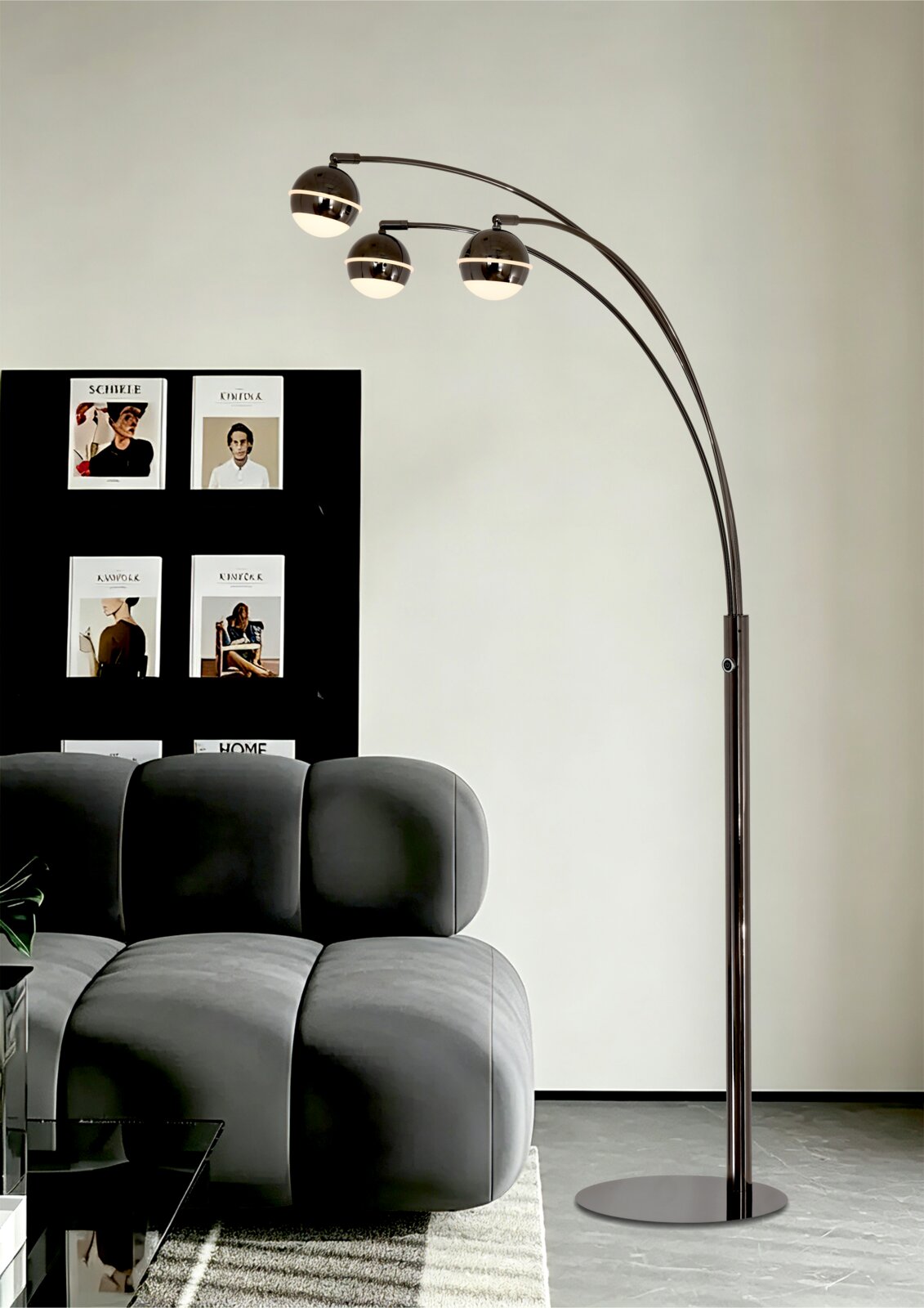 Moderne zwarte boogvloerlamp met drie gebogen armen en bolvormige lampenkappen, vanuit schuin vooraanzicht naast een grijze bank weergegeven